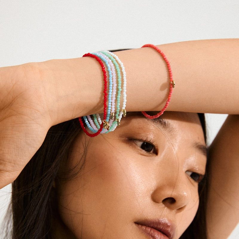Person wearing colorful beaded bracelets on a plain background
