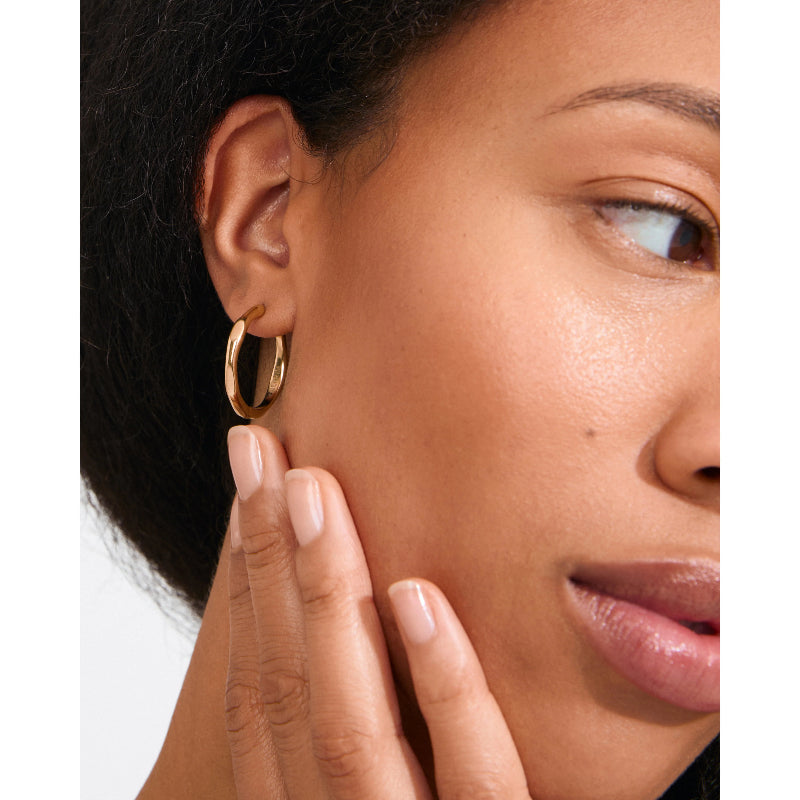Close-up of a woman wearing a gold hoop earring with a neutral background