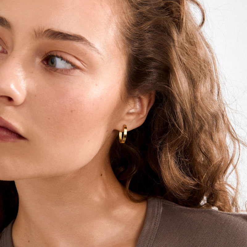 Close-up of a person wearing gold hoop earrings with a neutral background