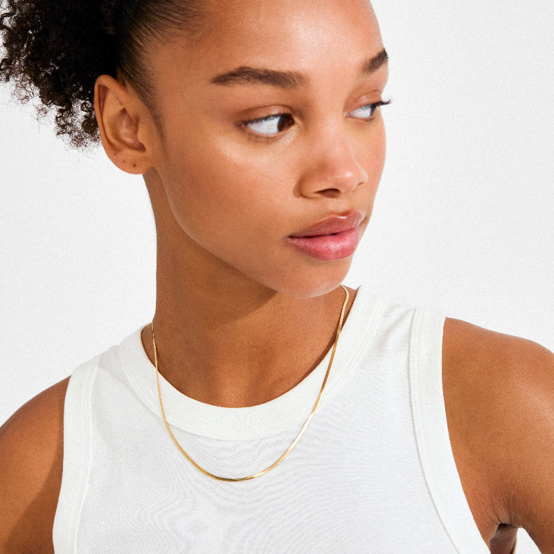 Woman wearing a white tank top and gold necklace on a plain background