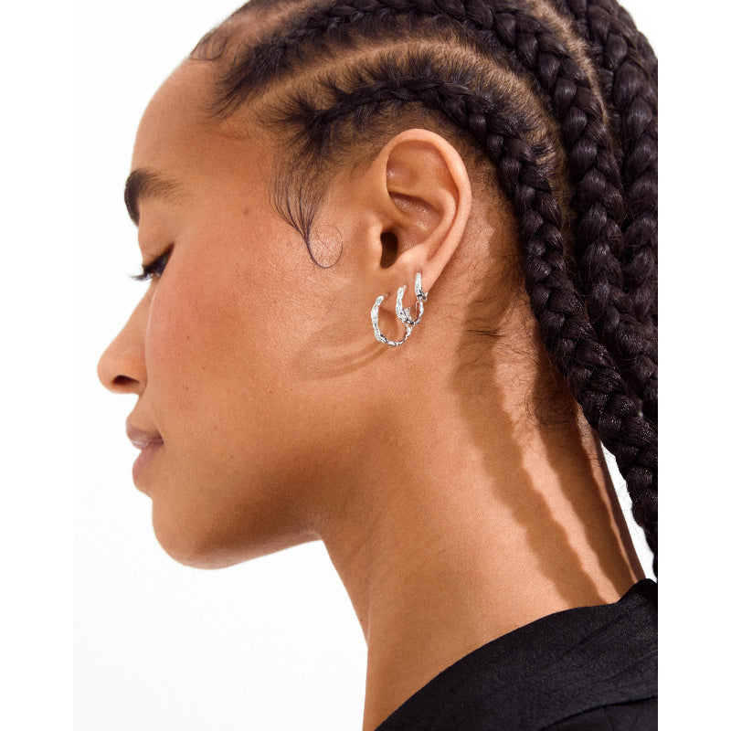 A close-up side profile of a model wearing a pair of silver crescent-shaped hoop earrings adorned with small clear stones, set against a plain white background.