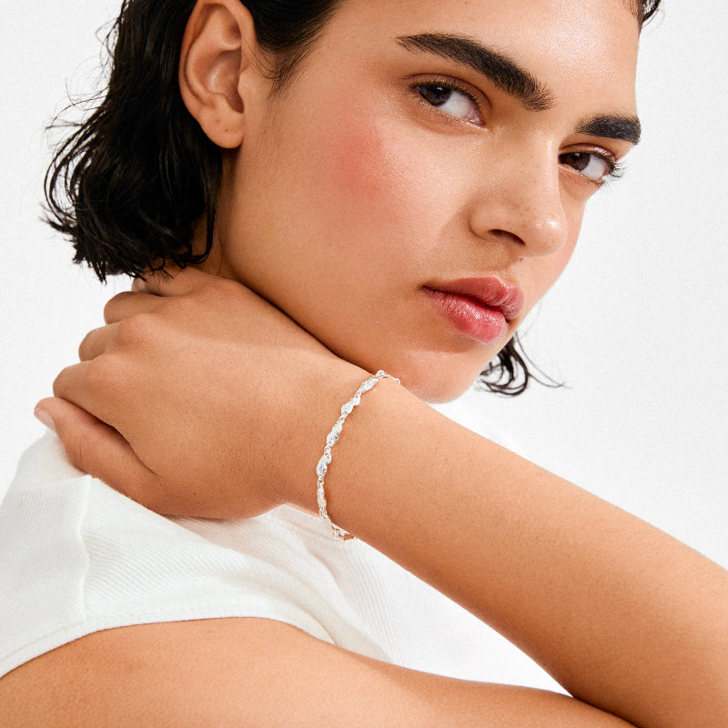 Silver coloured bracelet on a persons wrist on a white background