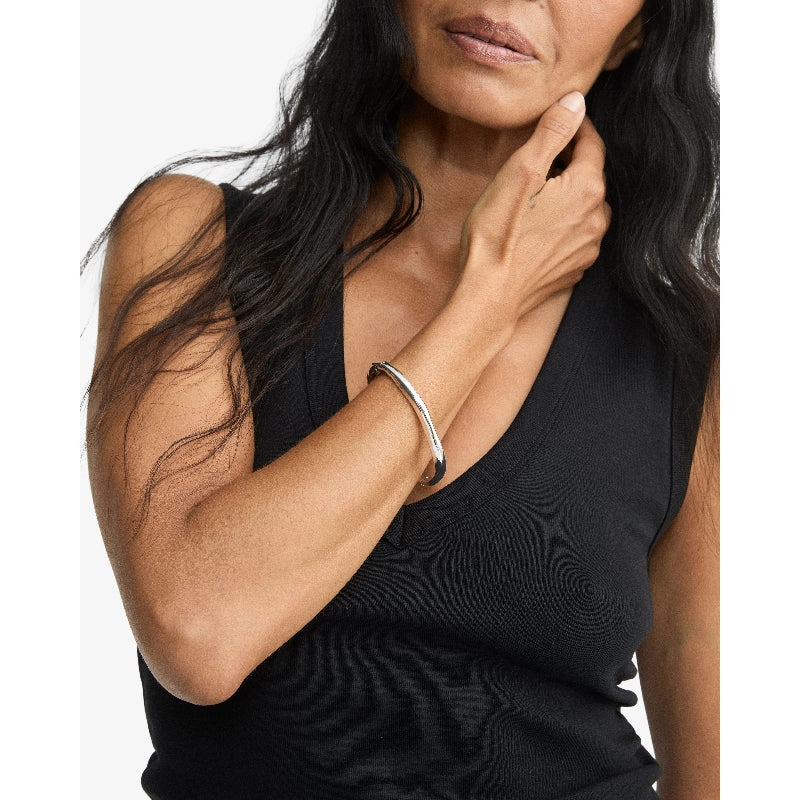 A close-up of a woman wearing a polished silver bangle bracelet with a black sleeveless top, set against a plain white background.