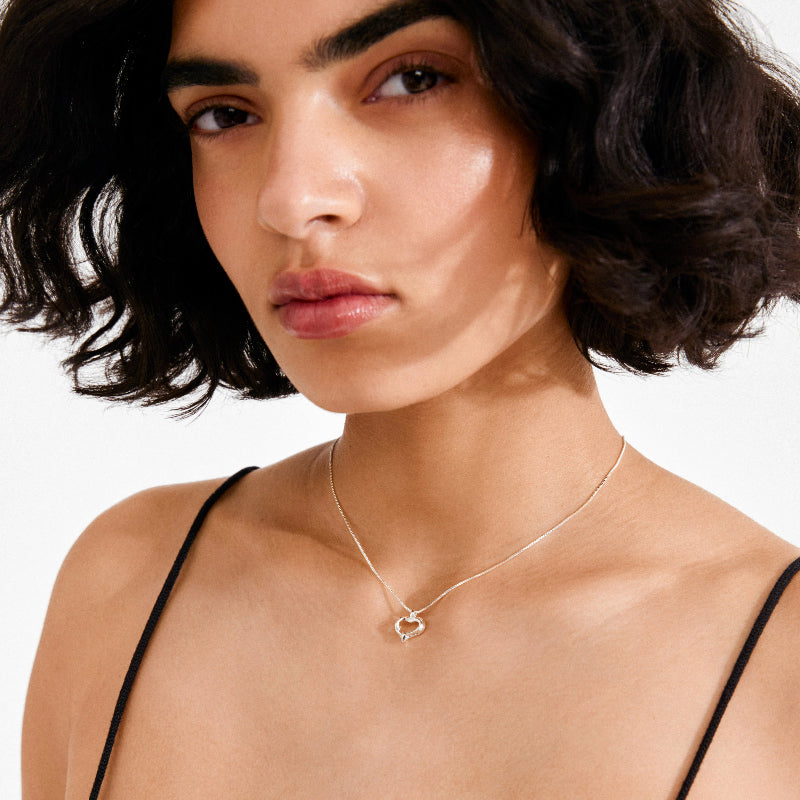 Close up of a woman wearing a heart necklace on a white background