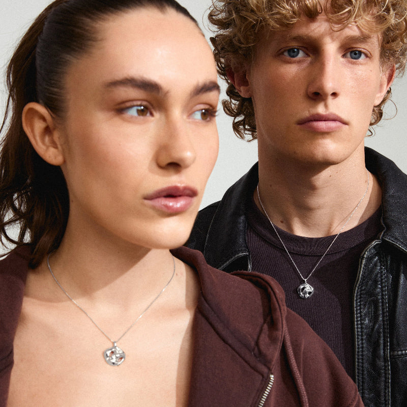 Two people wearing silver necklaces against a neutral background