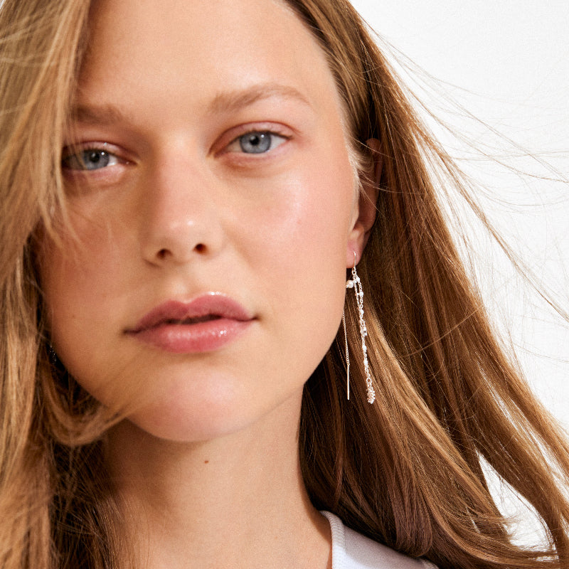 Close-up of a person with long hair wearing a dangling earring on a white background