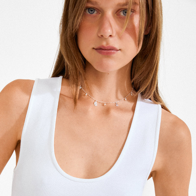 Woman wearing a white tank top and a delicate necklace on a plain background
