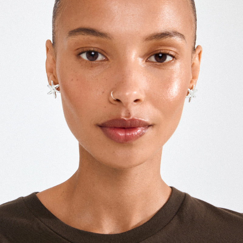 Silver starfish earrings on a woman against a white background