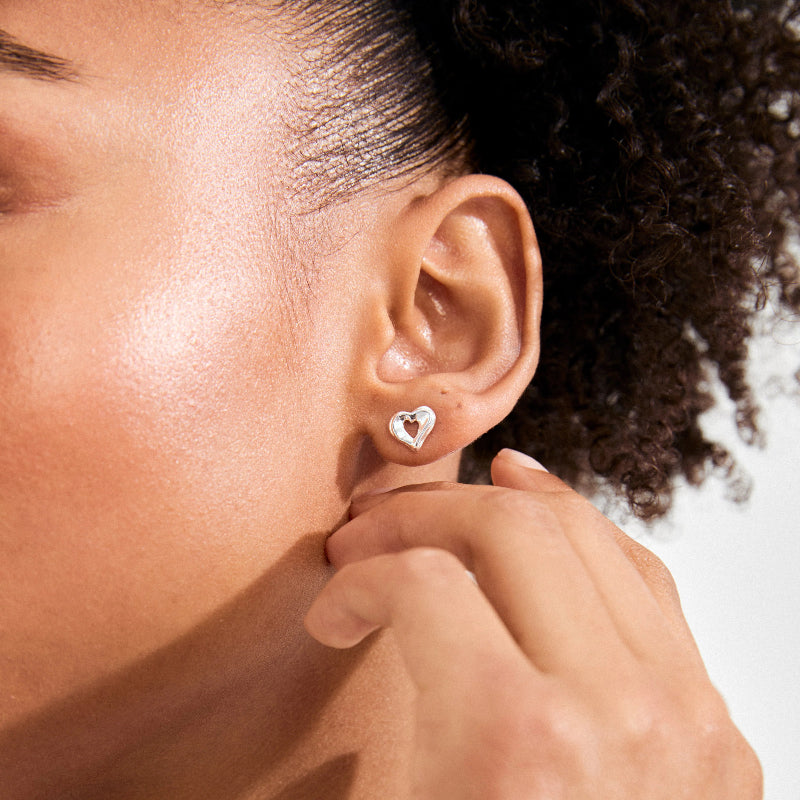 A person wearing a silver hear earring on a white background