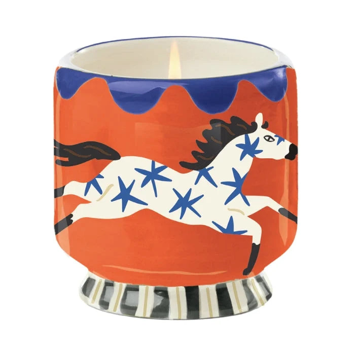 Candle in a decorative container with a horse design on an orange background
