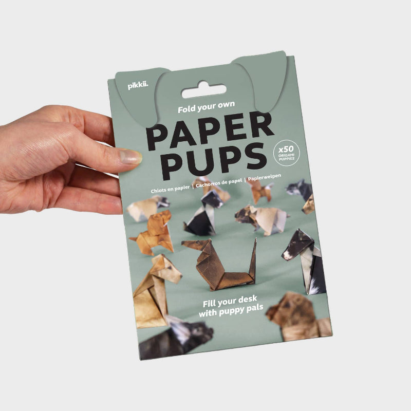 Packaging of paper puppets held by a hand with a light gray background