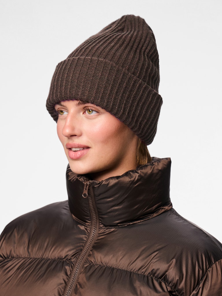 Person wearing a brown knit beanie and puffer jacket on a light gray background