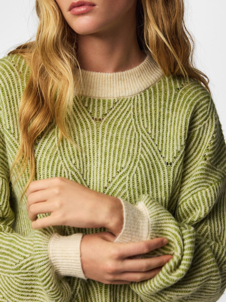 A close-up of a woman wearing a textured knit sweater with vertical wavy stripes in olive green and cream, featuring ribbed cream cuffs and collar.
