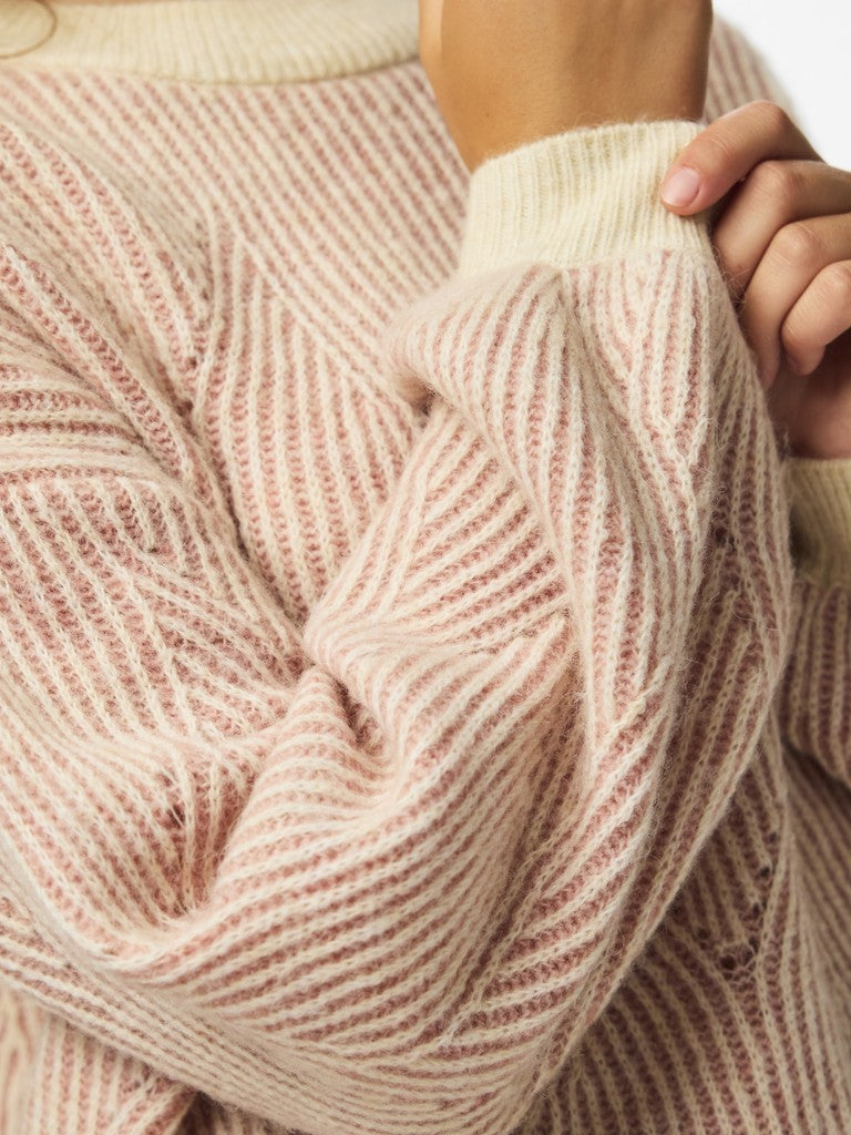 Close-up of a person wearing a soft knit sweater with vertical stripes in cream and dusty rose pink. The person is holding up the sleeve to show the texture and ribbed cuff.