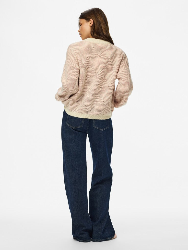 A woman shown from the back wearing a light beige textured knit cardigan and dark blue wide-leg jeans, standing against a plain white studio background.