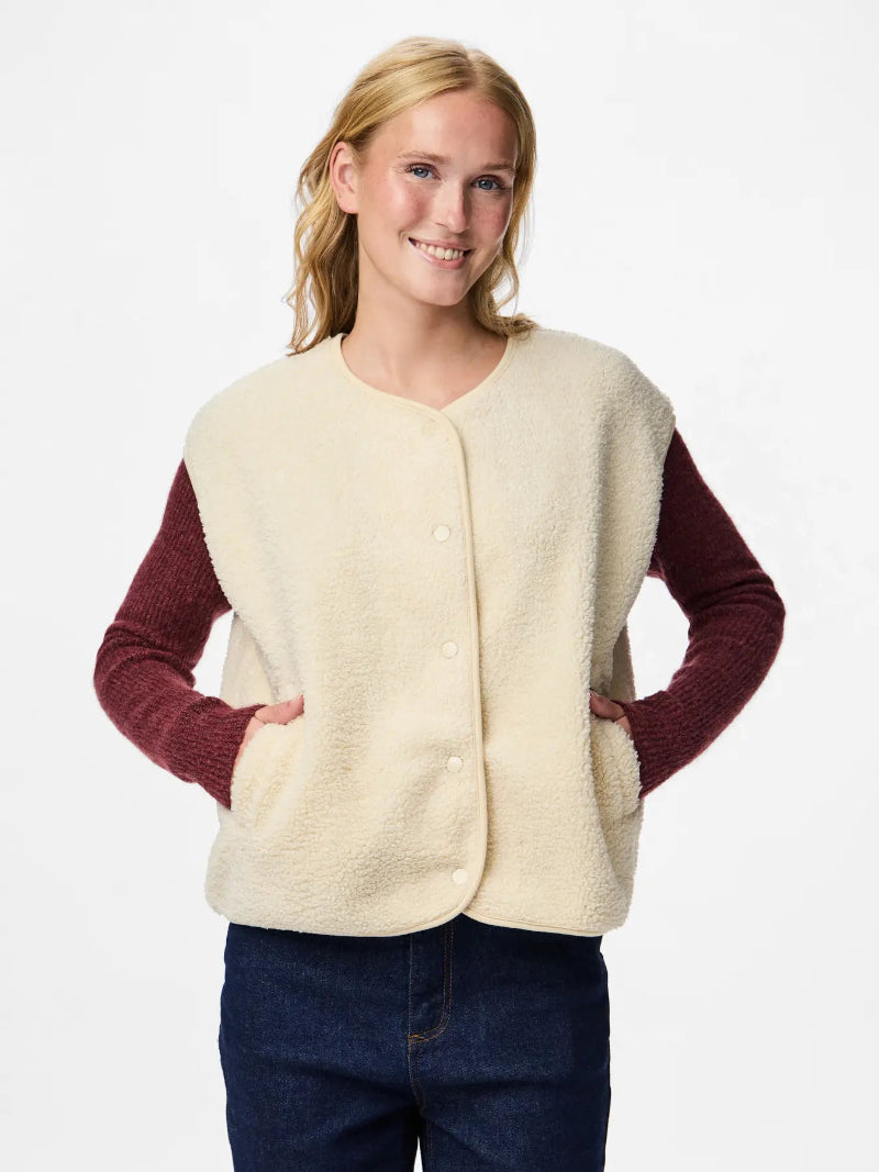 Woman wearing a cream-colored vest over a red long-sleeve shirt on a white background