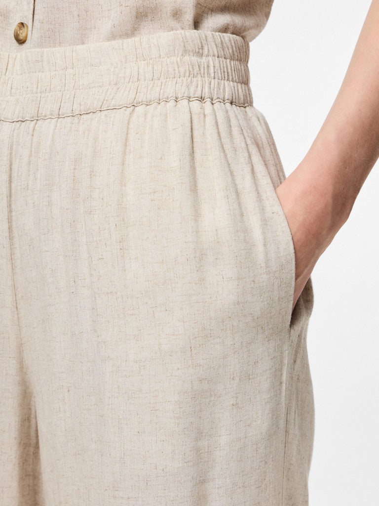 Close-up of a person wearing light beige linen trousers with an elastic waistband and side pocket, showing the fabric texture and a hand in the pocket.