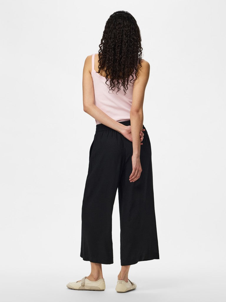 Woman wearing a pink sleeveless top and black wide-leg pants on a white background