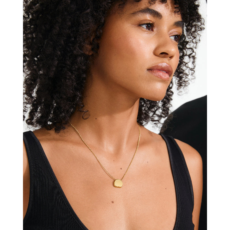 Woman wearing a gold necklace with a small pendant on a white background