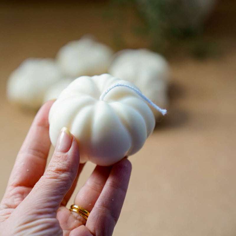 Hand holding a white candle shaped like a garlic bulb with more candles in the background.