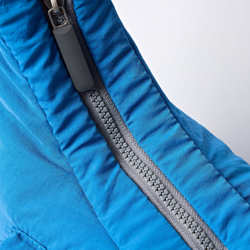 Close-up of a blue Roka Belize crossbody bag with a gray zipper on a white background
