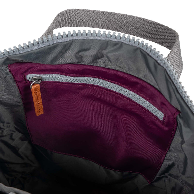 Roka Backpack Canfield Sustainable Medium Royal Burgundy Close-up of a gray backpack with a purple pocket and orange zipper pull.