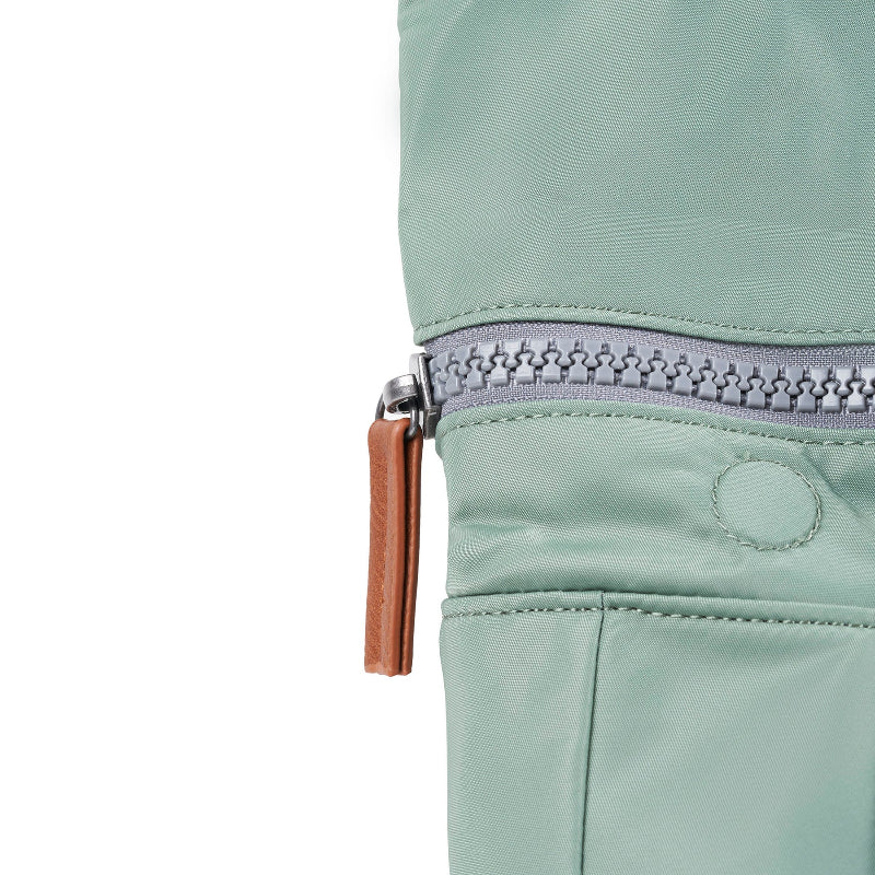 Close-up of a light green jacket with a zipper and brown pull tab on a white background