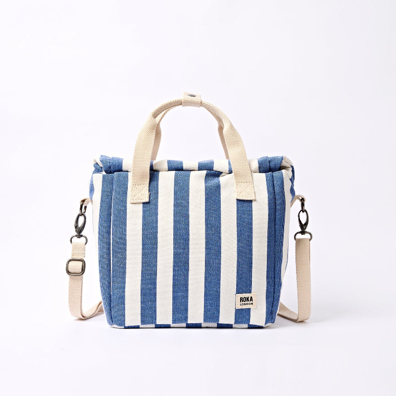 Roka Hampstead Lunch Bag Denim Stripe . Blue and white striped bag with beige handles and strap on a white background