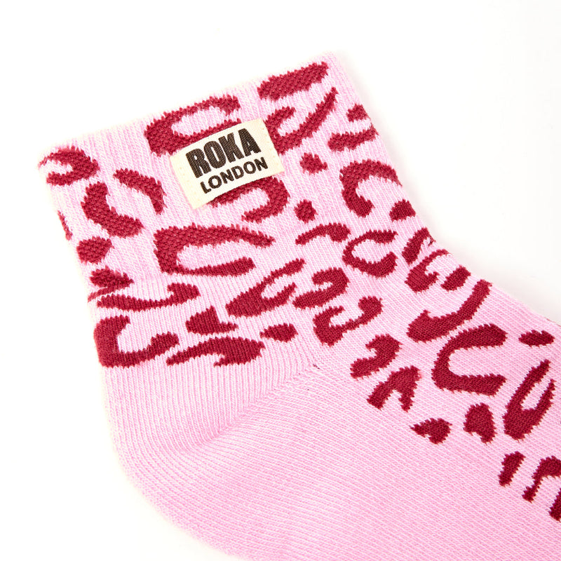 Pink sock with red leopard print pattern and Roka London label on a white background