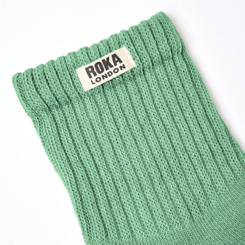 Green knitted sock with Roka London label on a white background