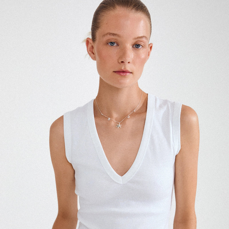 Woman wearing a white sleeveless top and a necklace with a starfish pendant on a plain background