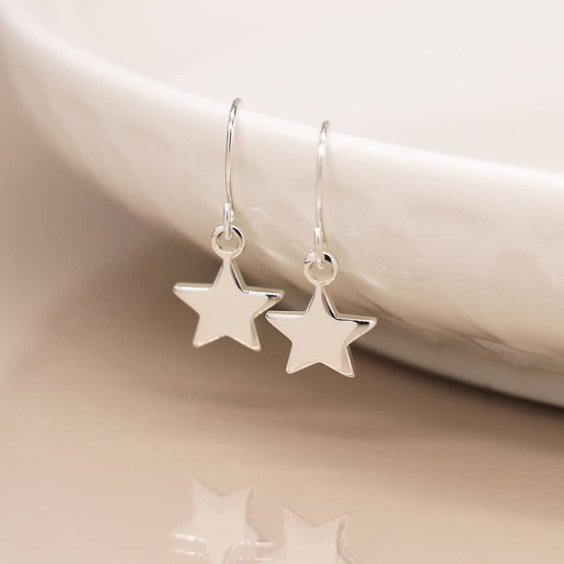 Silver star-shaped earrings on a neutral background