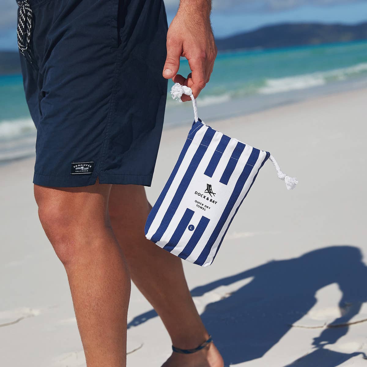Person holding a blue and white striped pouch on a beach