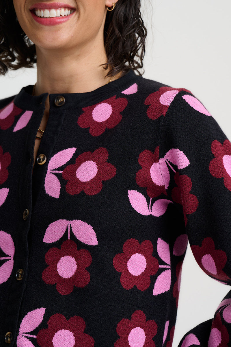 Close-up of a woman wearing a black knit top with a bold pink and burgundy floral pattern, featuring a buttoned neckline.