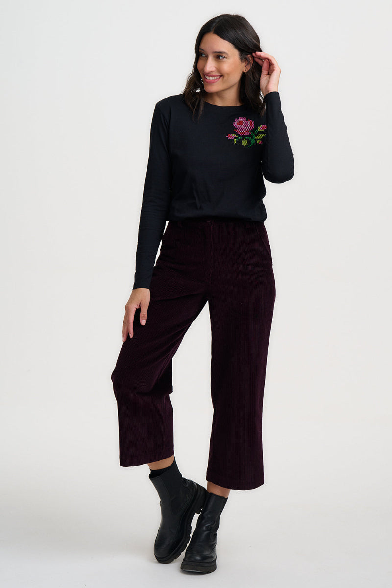 Woman wearing a black sweater with floral embroidery and dark pants on a white background