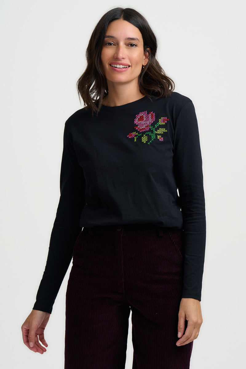 Woman wearing a black long-sleeve shirt with a floral embroidery design on a white background
