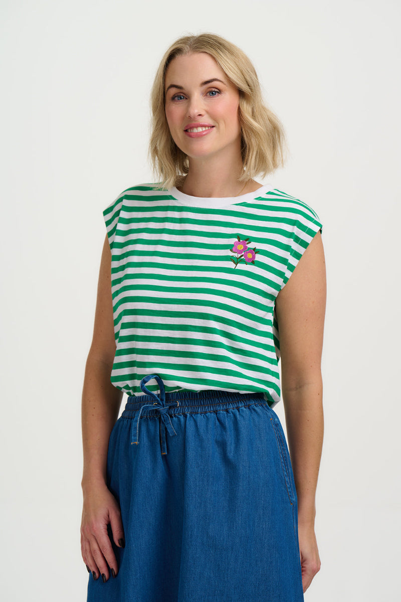 Woman wearing a green and white striped sleeveless top with a floral design, standing against a plain background.