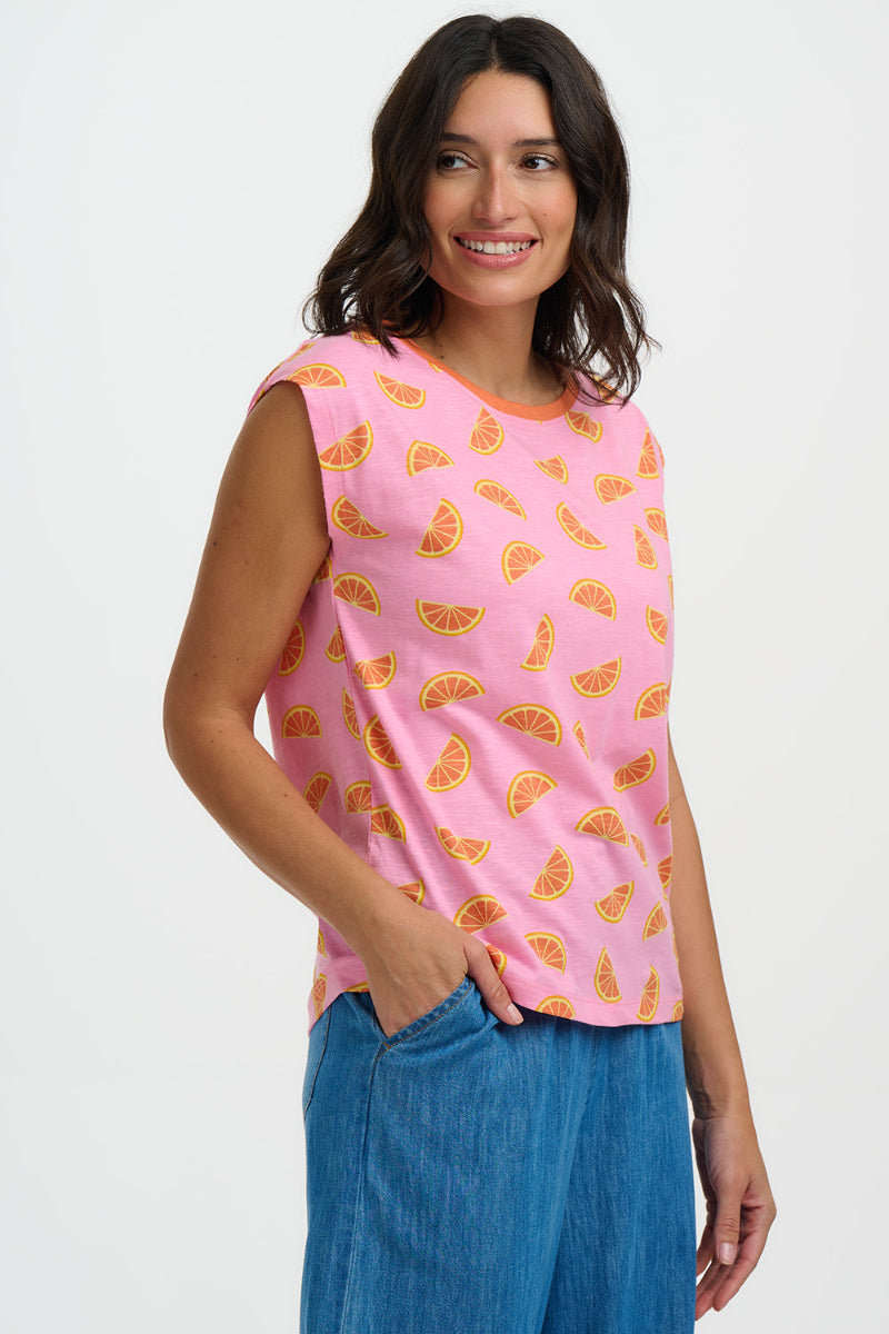 Woman wearing a pink sleeveless top with orange fruit pattern and blue pants on a white background
