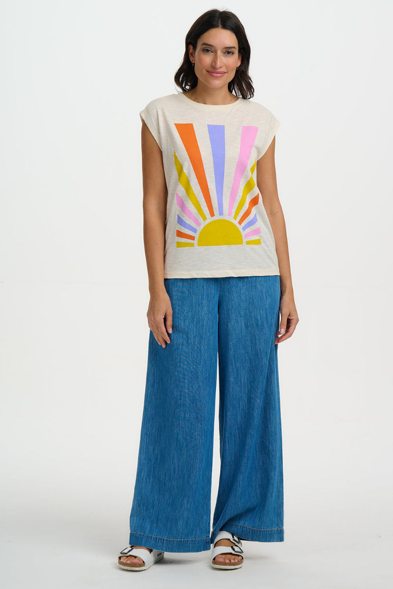 Woman wearing a colorful sun graphic t-shirt and blue pants on a white background