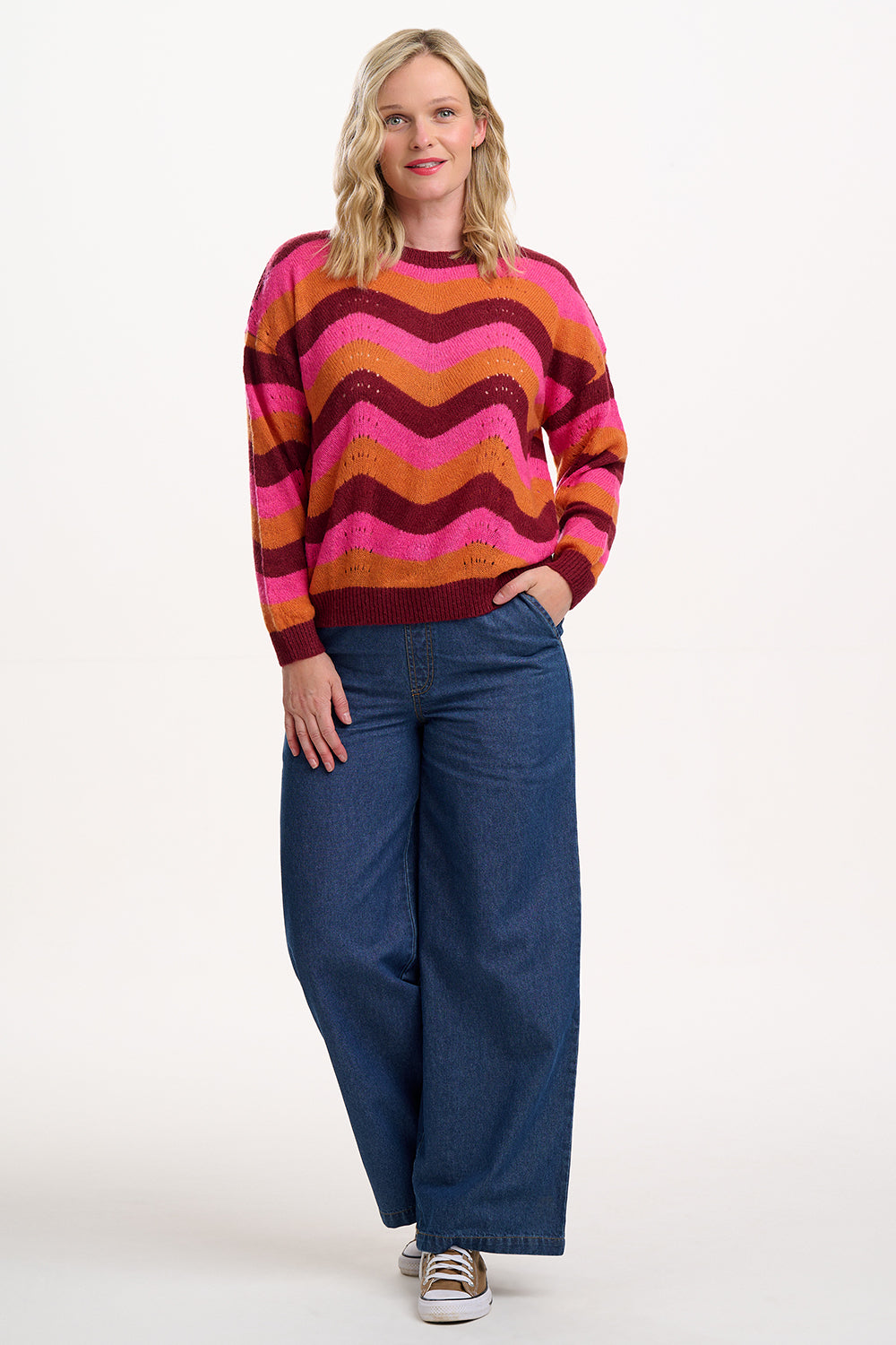 Woman wearing a colorful striped sweater and blue jeans on a white background