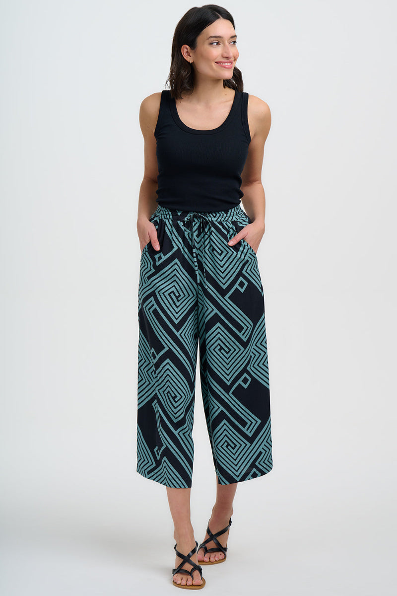 Woman wearing a black tank top and patterned pants on a white background
