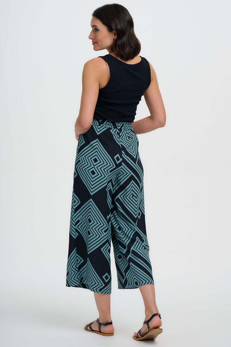 Woman wearing a black sleeveless top and teal patterned pants on a white background