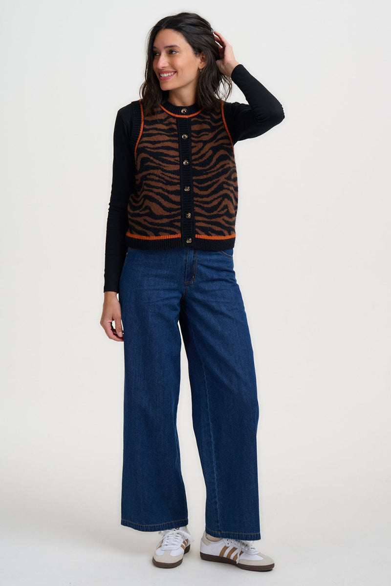 Woman wearing a black top under a orange zebra pattern waistcoat and blue jeans on a white background