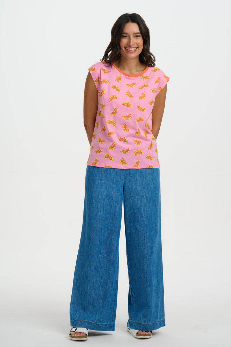 Woman wearing a pink sleeveless top with orange patterns and blue jeans on a white background