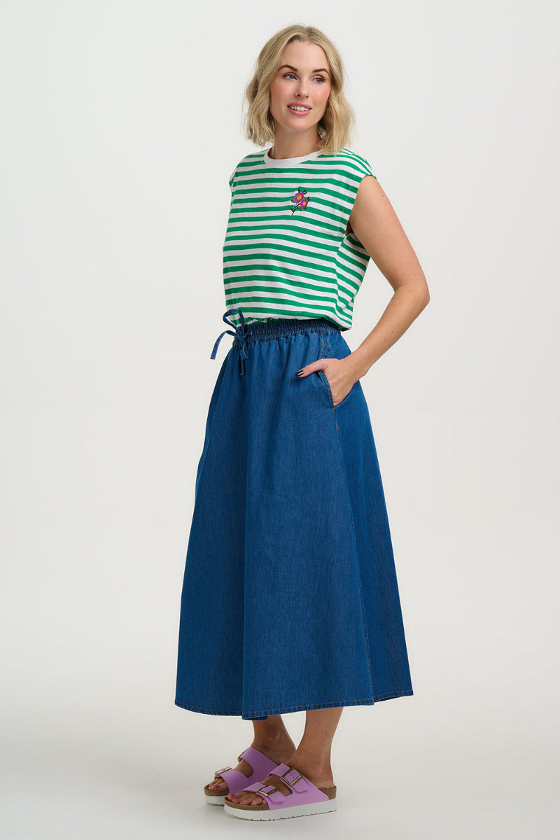 Woman wearing a green and white striped sleeveless top with a blue skirt on a white background