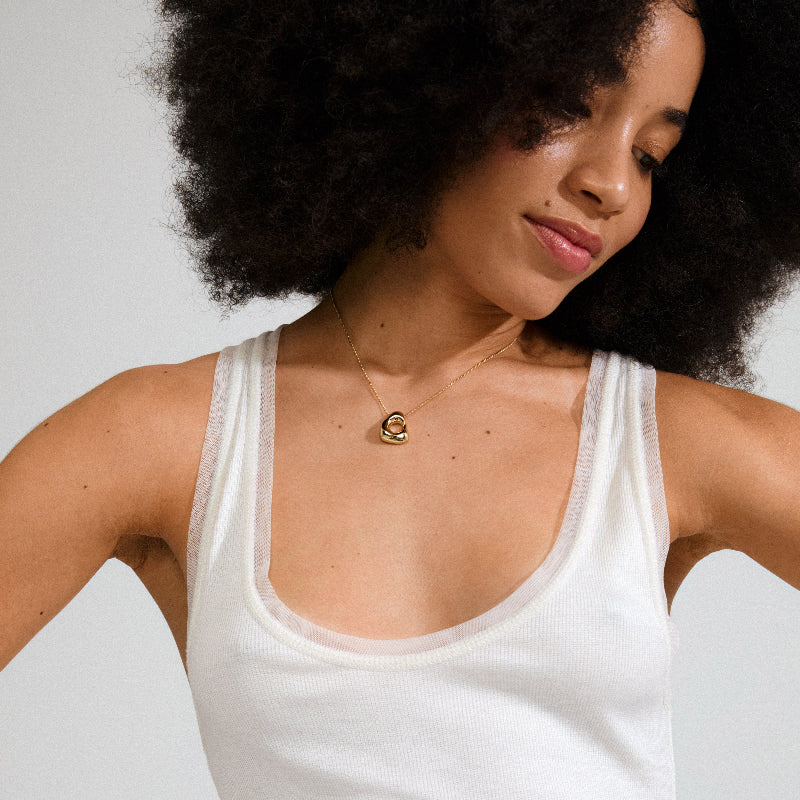 Woman wearing a white tank top with a gold necklace against a neutral background