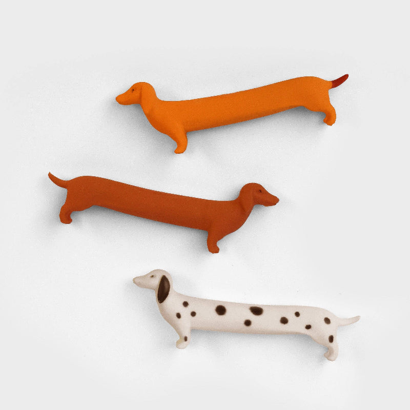 Three Dog Erasers in orange, brown, and white with black spots on a light grey background.