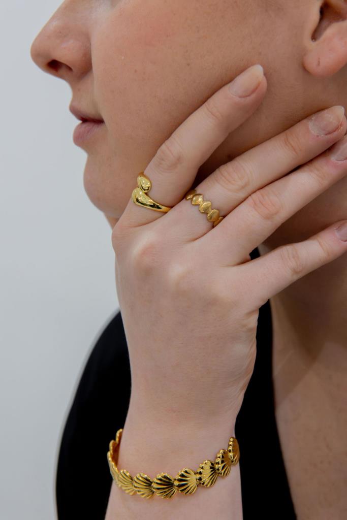 Close-up of a person wearing gold rings and a bracelet on a plain background