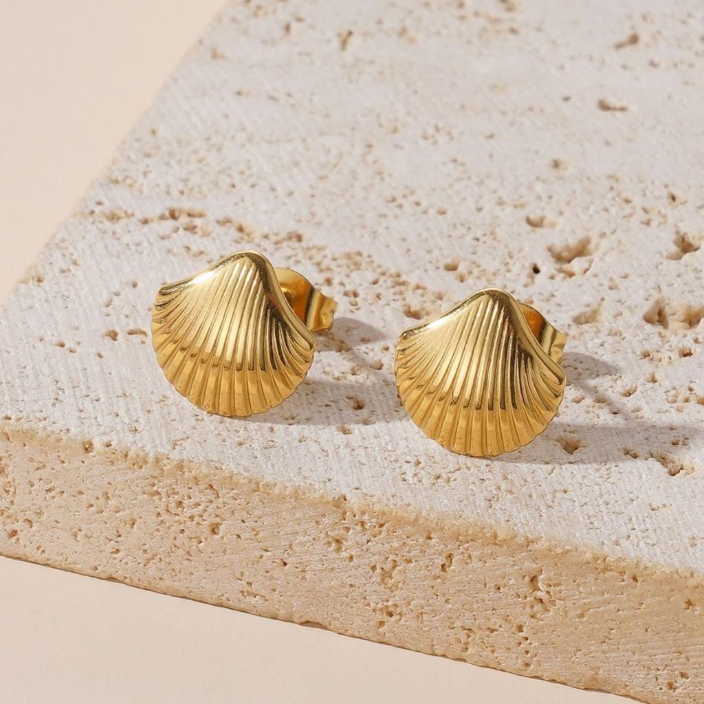 Gold shell-shaped earrings on a textured stone surface