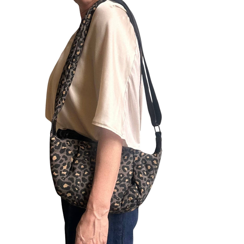 A person wearing a beige short-sleeve top and dark blue jeans carries a leopard-print shoulder bag with a black strap against a plain white background.